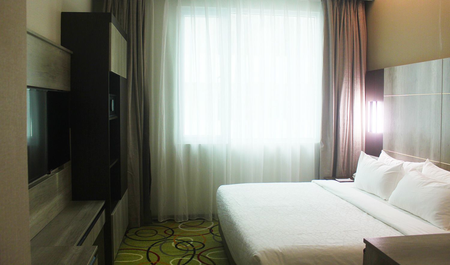 Ein Hotelzimmer mit Bett, Fernseher und einem Fenster mit Vorhängen.
