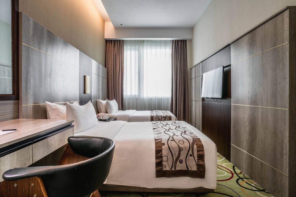 Una habitación de hotel con cama, escritorio, silla, televisor y ventana con cortinas.