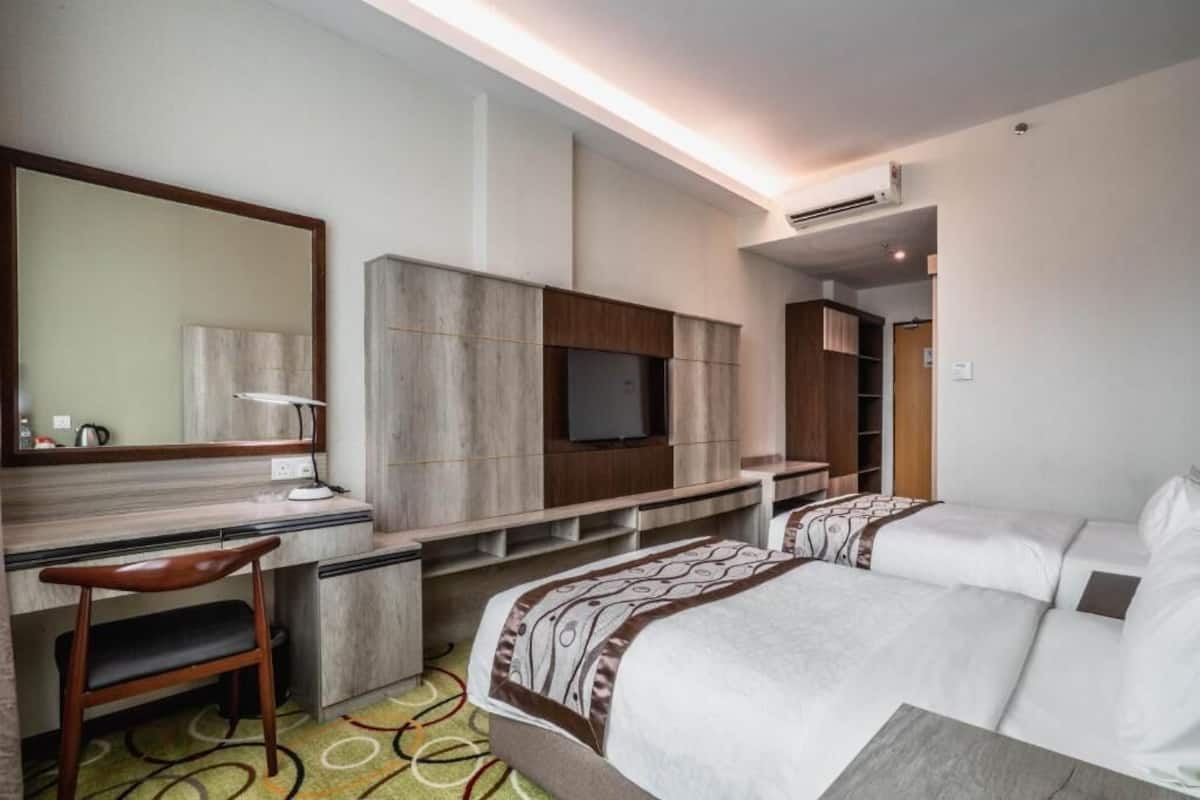 Habitación de hotel con escritorio, silla, dos camas, televisor y almacenamiento integrado.