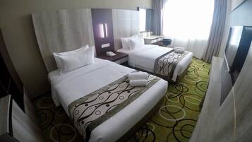 A hotel room with two beds, a desk, a chair, a TV, and a window with curtains.