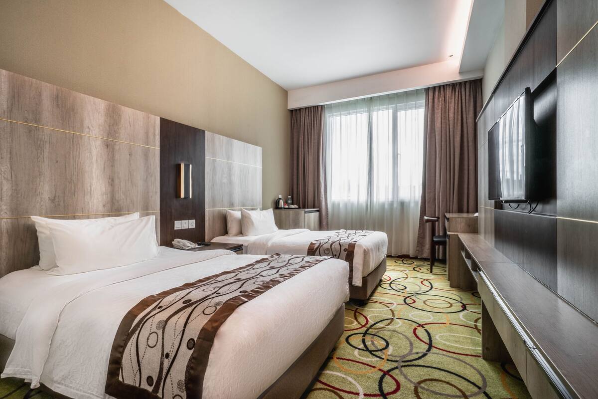 Habitación de hotel con dos camas, televisión, escritorio y un ventanal grande con cortinas.