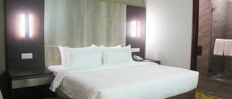 A hotel room with a large bed, a desk with a phone, and a shower area.