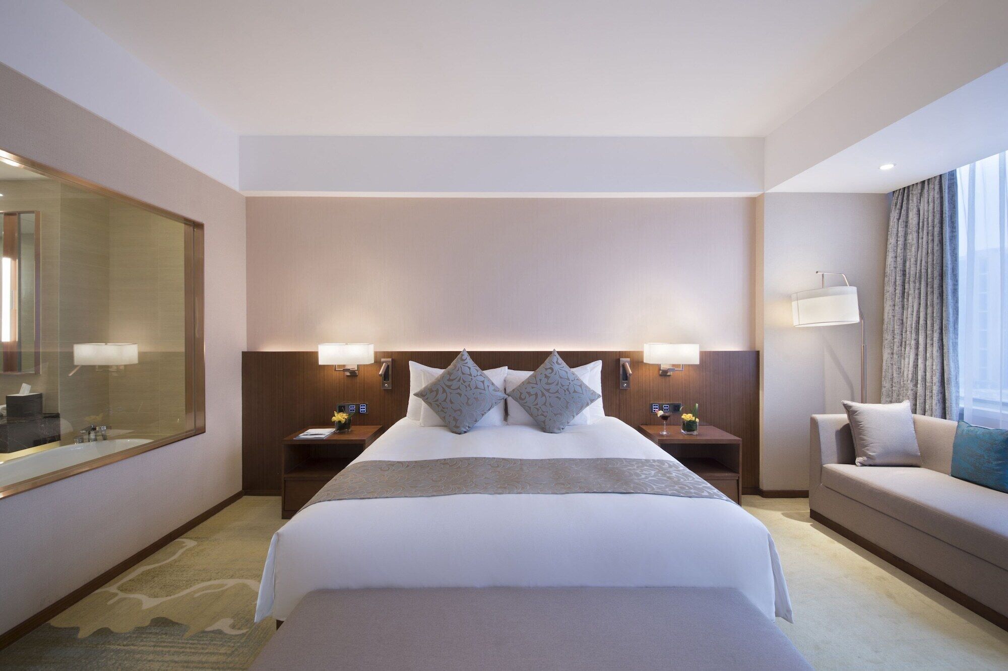 A hotel room with a large bed, two bedside tables with lamps, a sofa, and a large mirror.