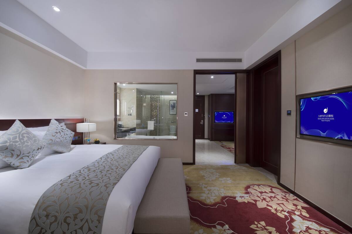 Een hotelkamer met een groot bed, een televisie, een spiegel en een zichtbare badkamer door een open deur.