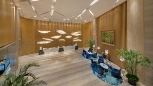 Een moderne lobby met een receptiebalie, zithoek en een groot schilderij aan de muur.