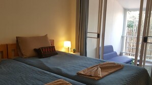 A hotel room with two beds, a nightstand with a lamp, and a view of the outside balcony. - The Commonroom CNX (Chiang Mai)