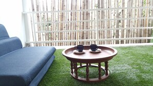A round wooden table with two cups on saucers, a blue sofa, and a bamboo fence in the background. - The Commonroom CNX (Chiang Mai)