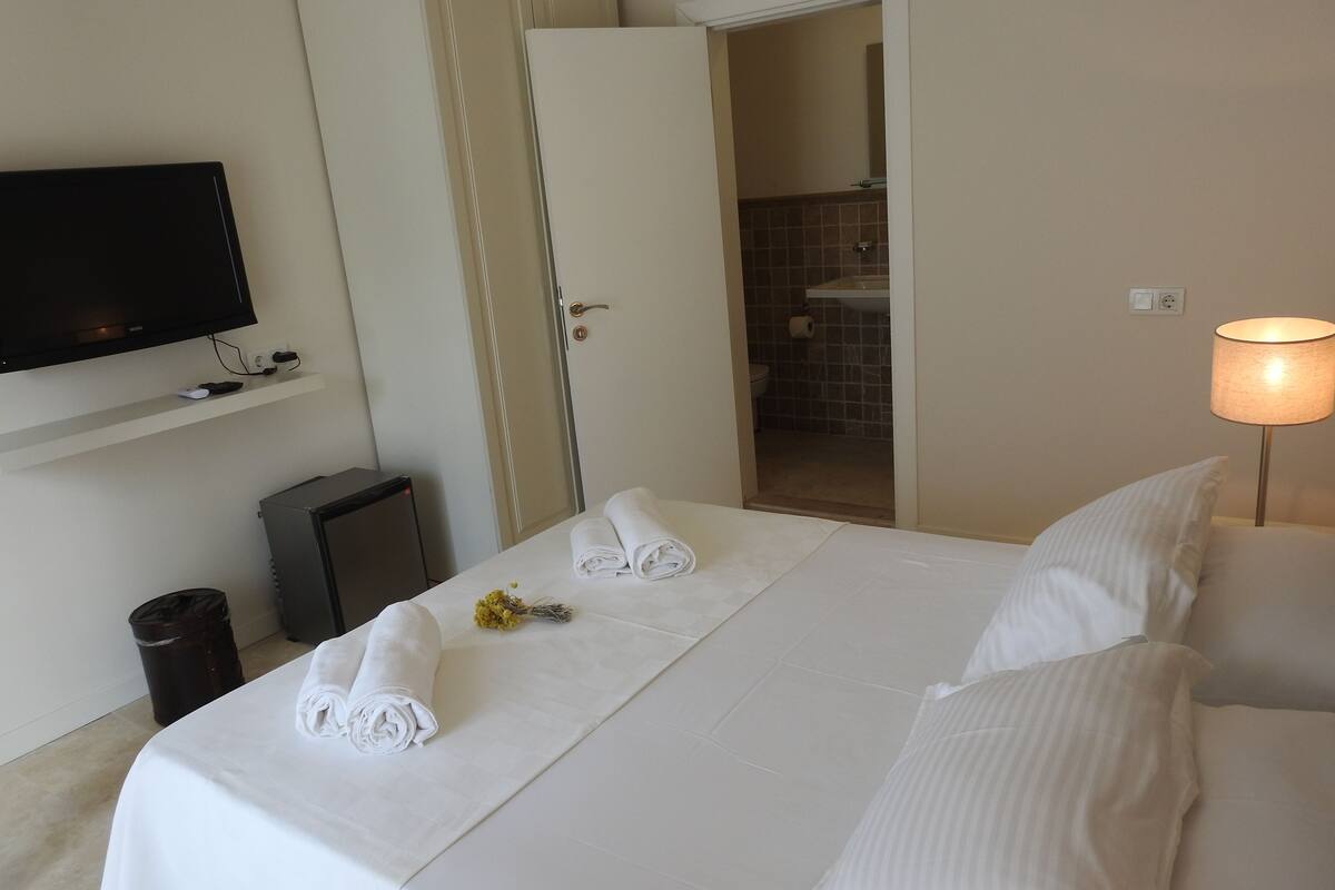 A hotel room with a bed, a TV, a lamp, and a bathroom visible through an open door.