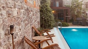 Un área junto a la piscina con sillones de madera y una pared de piedra.