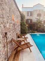 Zona de piscina con sillas de madera y una pared de piedra.