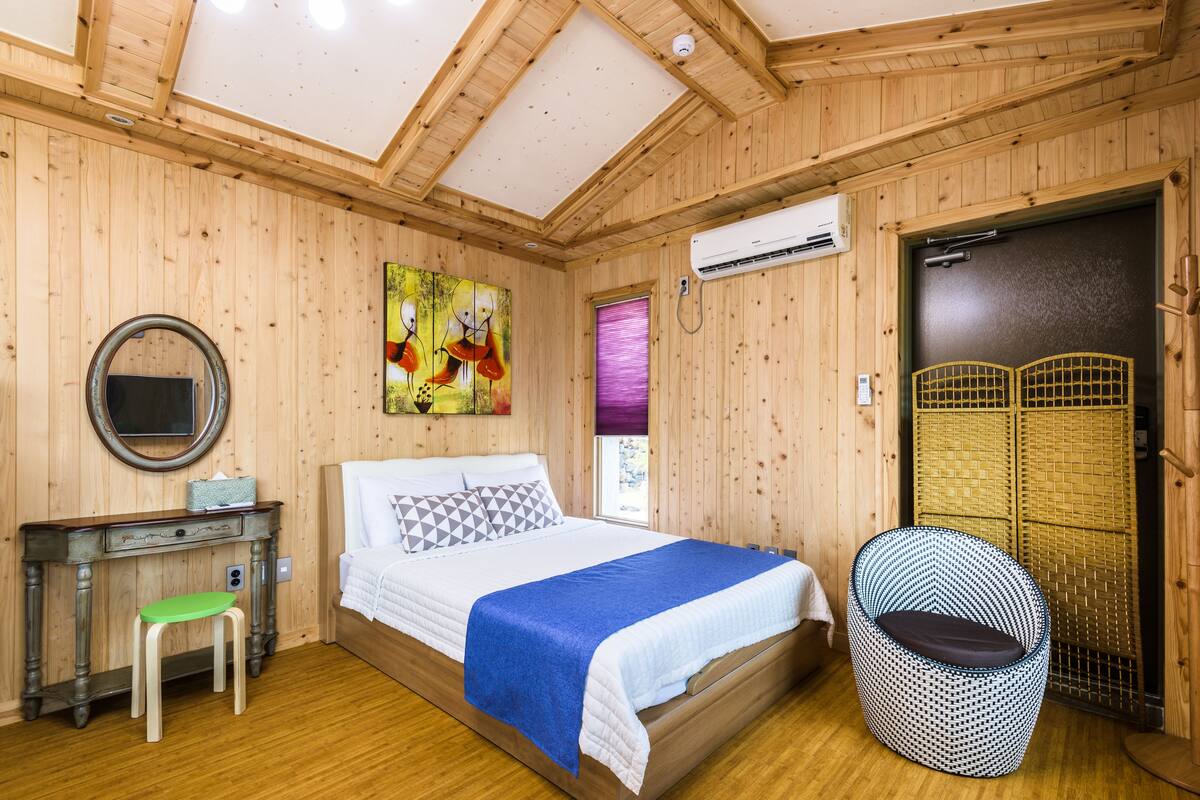 A wooden-paneled room with a bed, a desk, a chair, and an air conditioning unit.