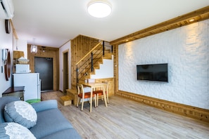 A modern living room with a wooden staircase, a dining area, and a kitchen.