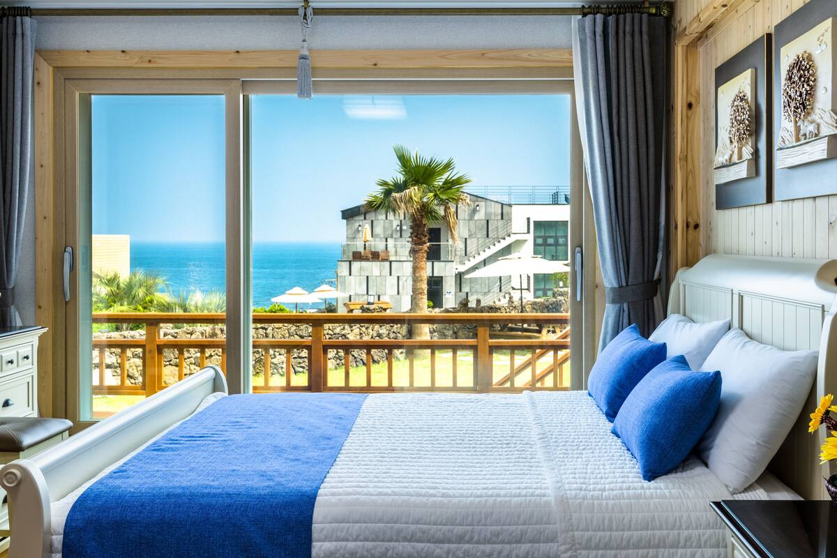 A bedroom with a large bed, a view of the ocean, and a balcony with a wooden railing.