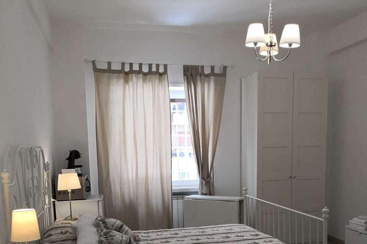 A bedroom with a bed, nightstands, a lamp, a chandelier, and a window with curtains.