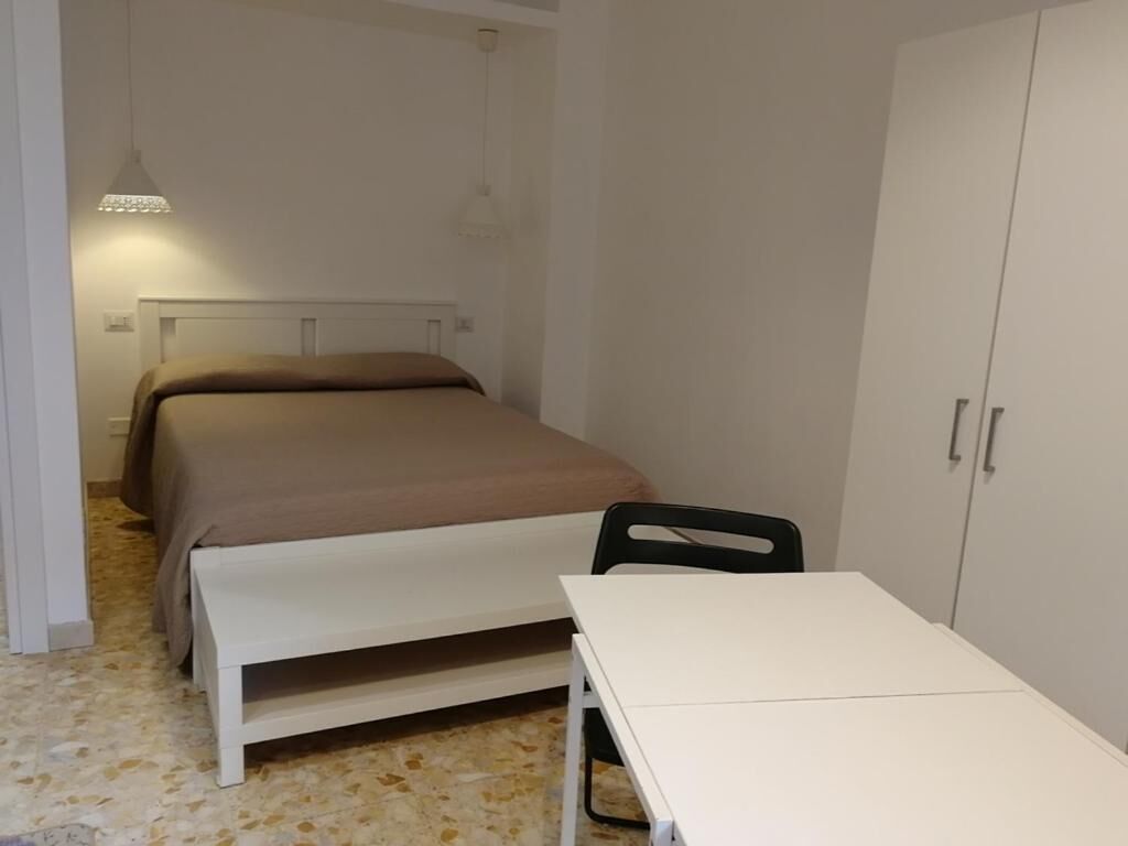 A bedroom with a bed, a white table, a chair, and a wardrobe.