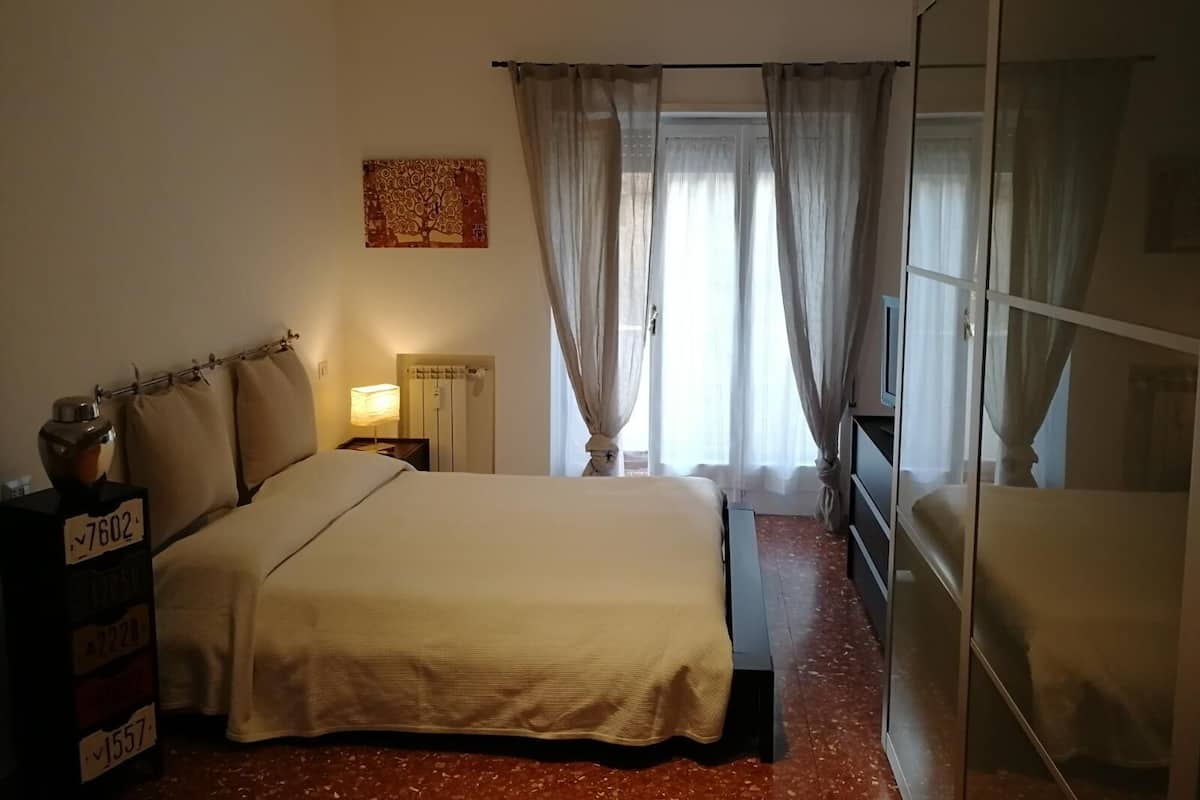 A hotel room with a bed, a bedside table with a lamp, a wardrobe, and a window with curtains.