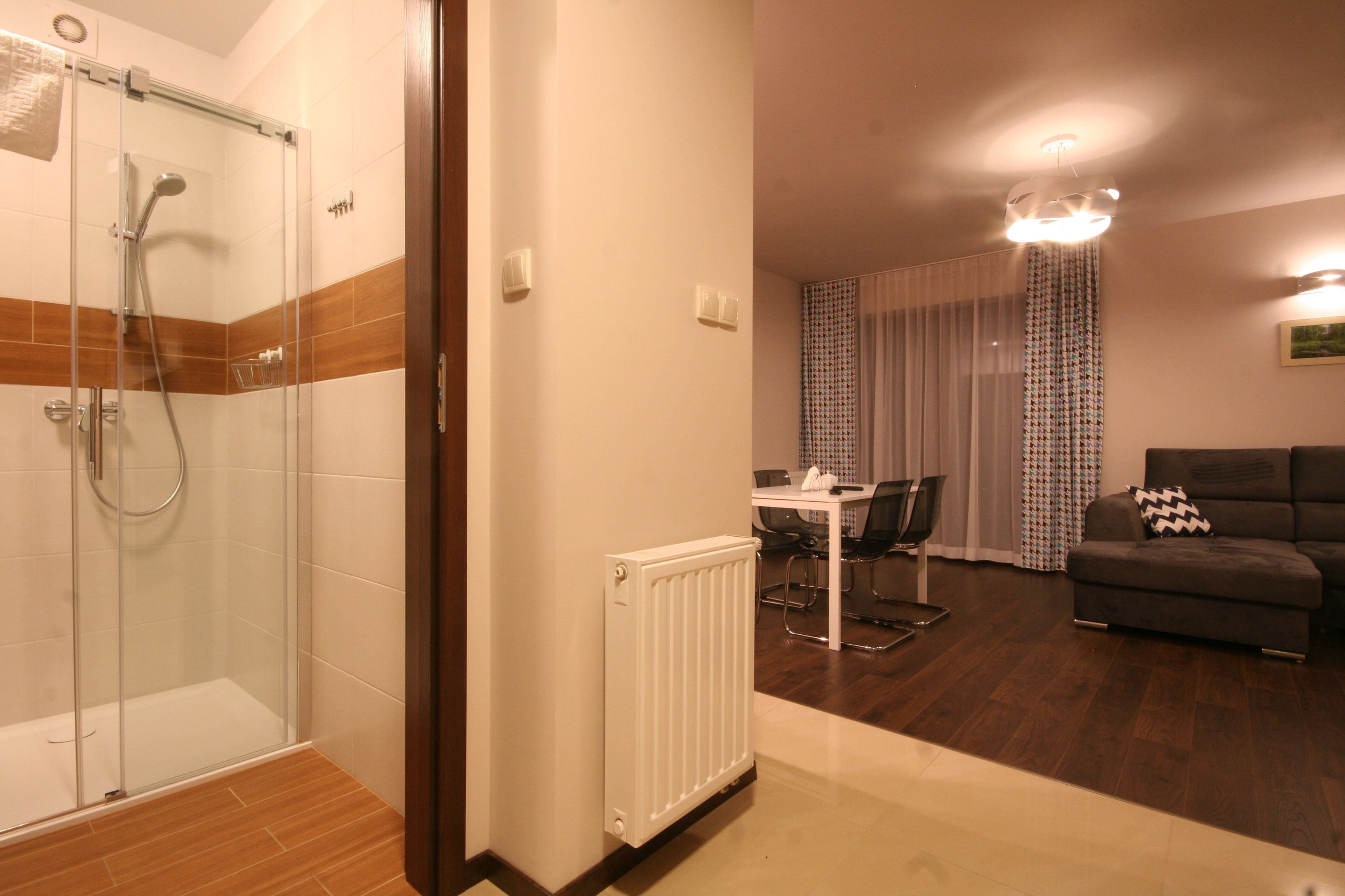 A modern bathroom with a glass shower enclosure, a white radiator, and a wooden floor.