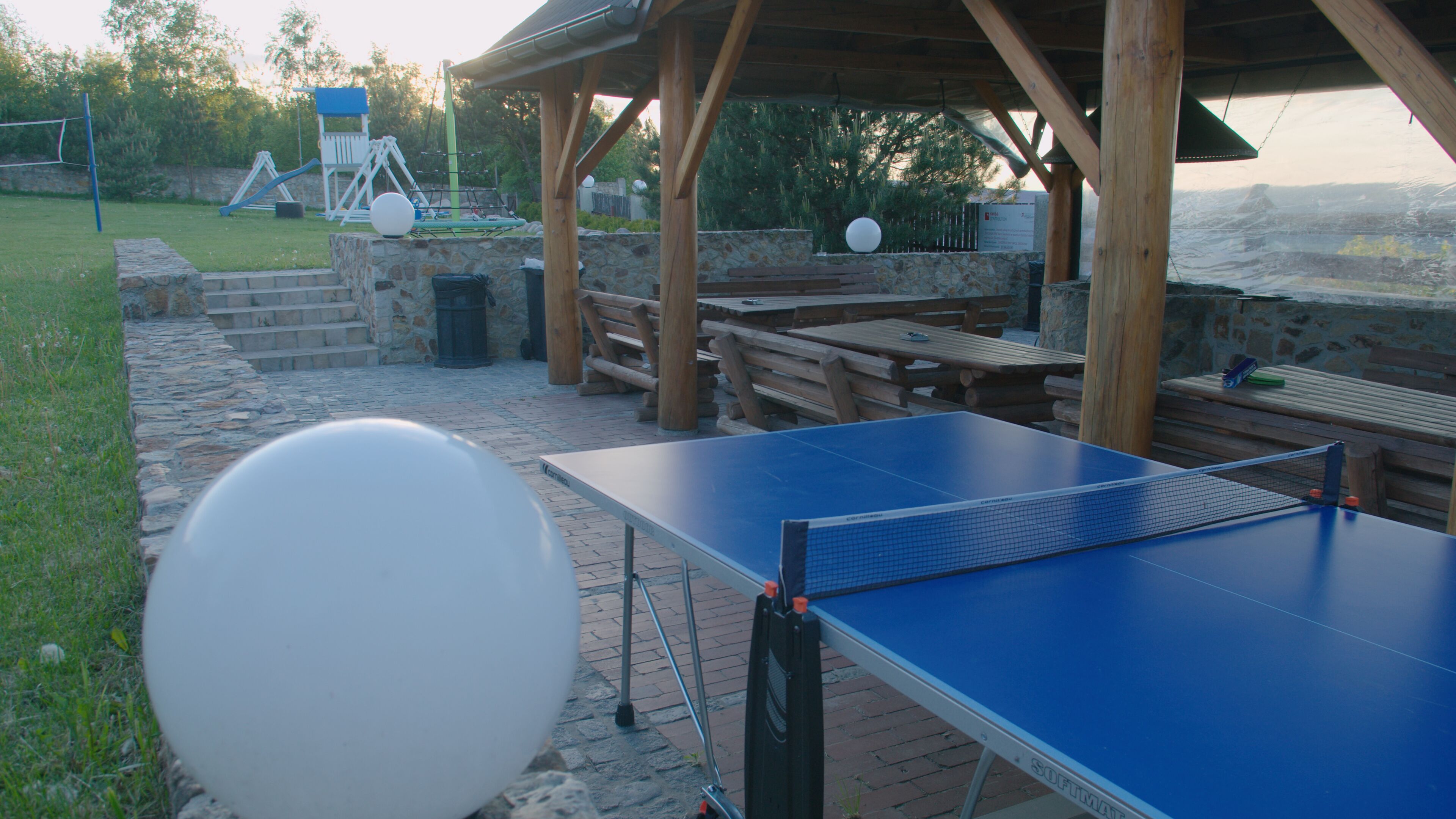 An outdoor table tennis table with a wooden pavilion in the background.