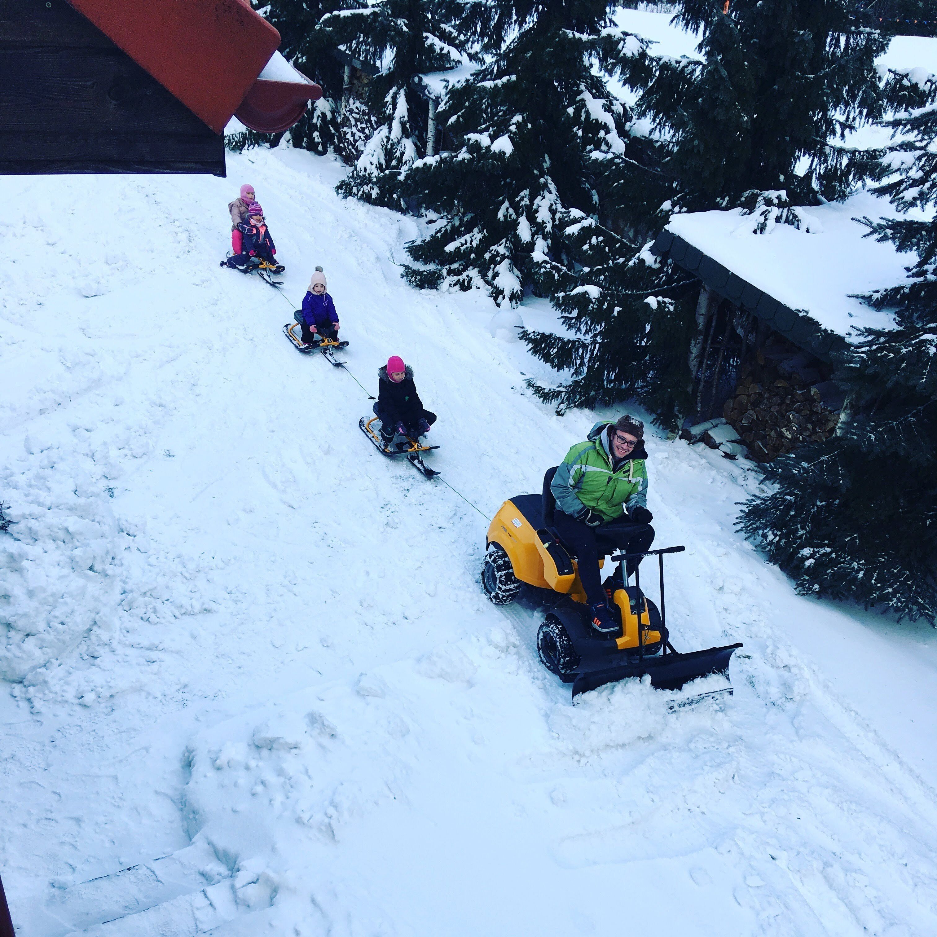 Pendiente nevada con personas en trineo y un vehículo de nieve.