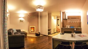 Ein modernes Wohnzimmer mit Kamin, einem Essbereich mit Tisch und Stühlen sowie einer Küche mit Flachbildfernseher.