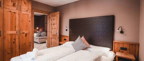 A double bed with white linens and a headboard, wooden wardrobe, and bedside tables.