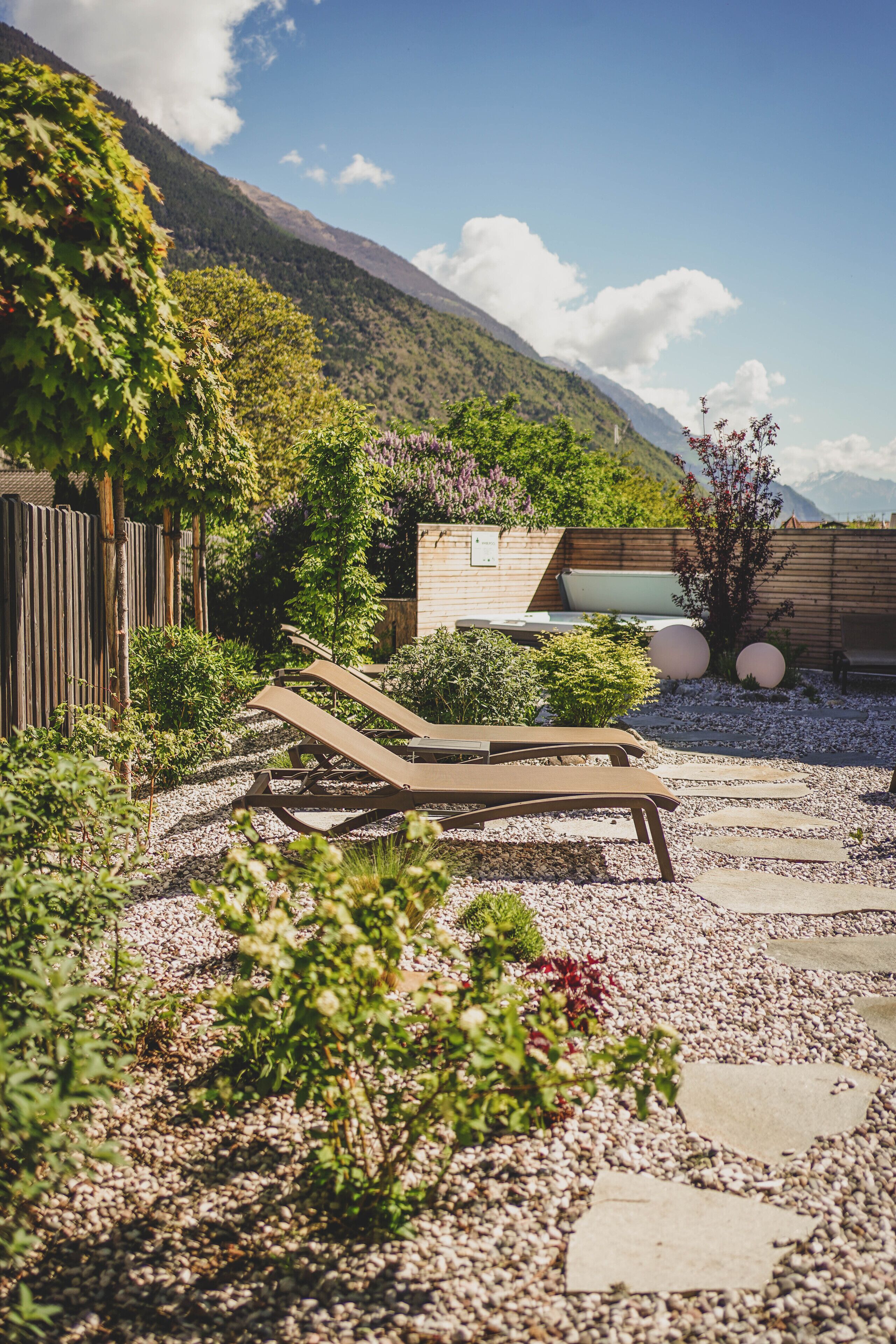 Un jardin doté d’une terrasse en bois, de chaises longues et offrant une vue sur les montagnes.