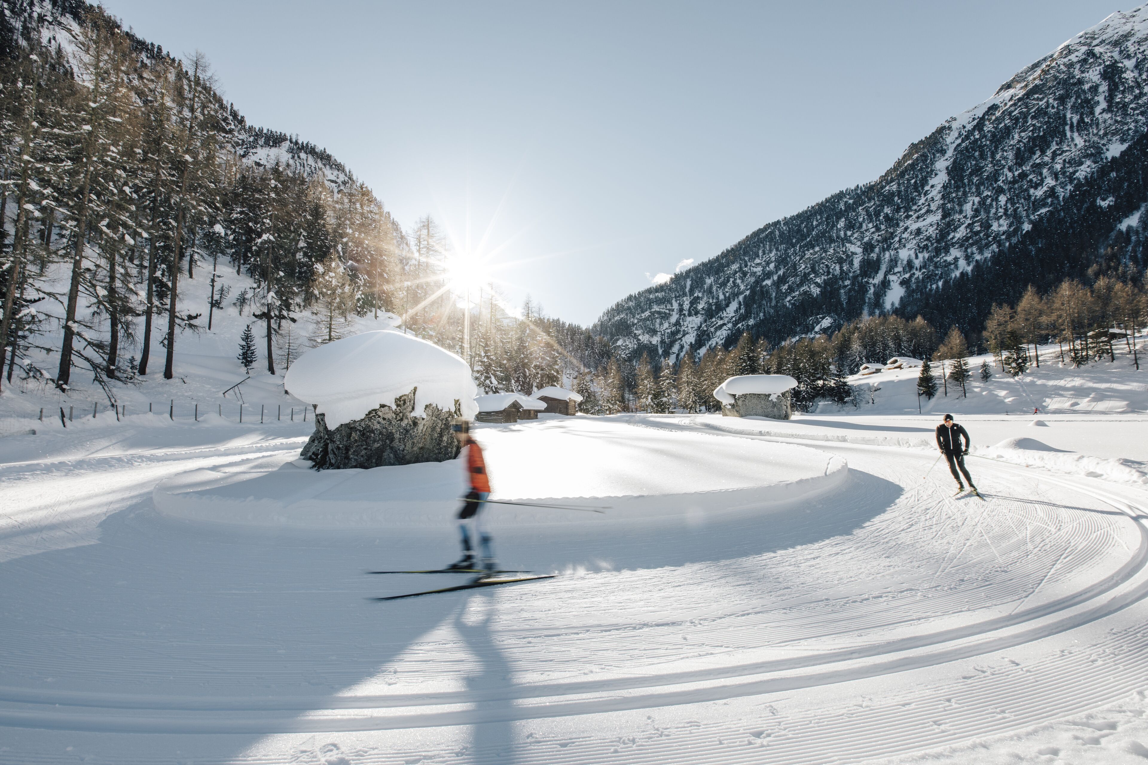 Una pista da sci innevata con sciatori, cielo sereno e montagne sullo sfondo.