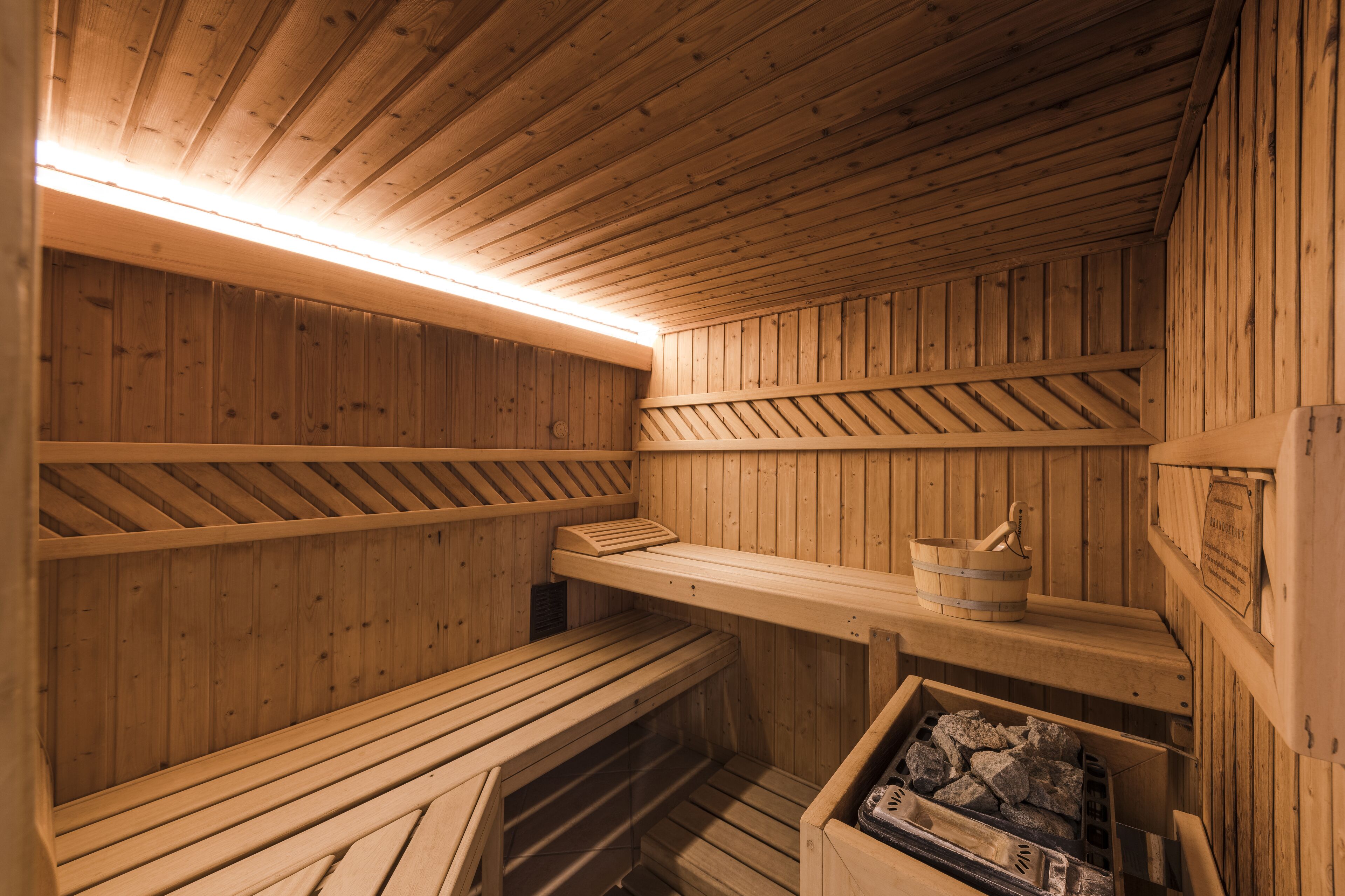Un sauna en bois, avec des bancs, un seau et un poêle à bois.