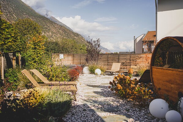 Un jardín con un sendero de piedra, sillones de madera y una valla de madera.