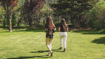 A grassy outdoor area with chairs, two people walking, and a mountainous backdrop.