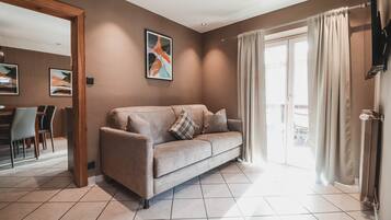 A modern living room with a beige sofa, a dining area with chairs, and a large window with curtains.