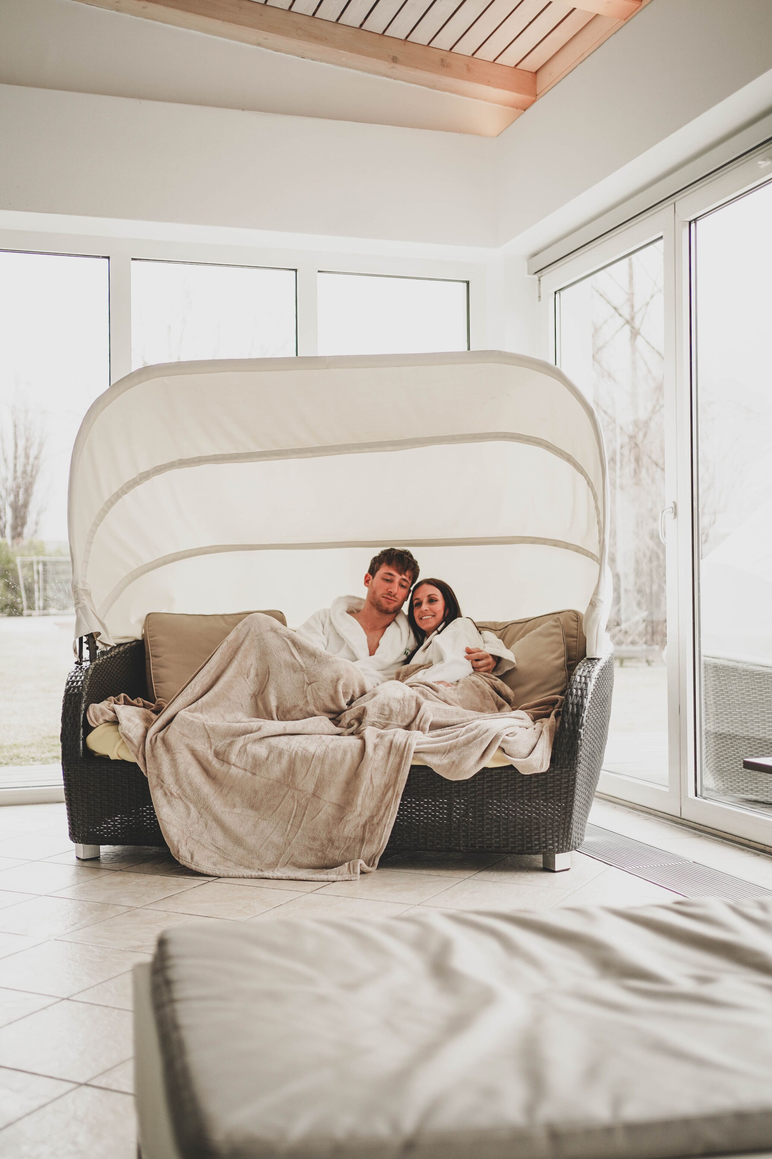 A couple in a cozy, covered outdoor seating area with a view of the outdoors.