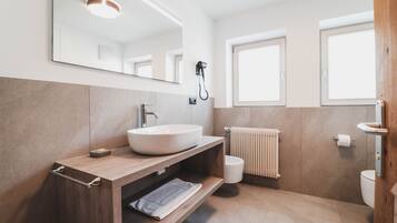 Une salle de bain moderne avec un grand miroir, un meuble-lavabo en bois, un lavabo blanc, un porte-serviettes, des toilettes et une fenêtre.