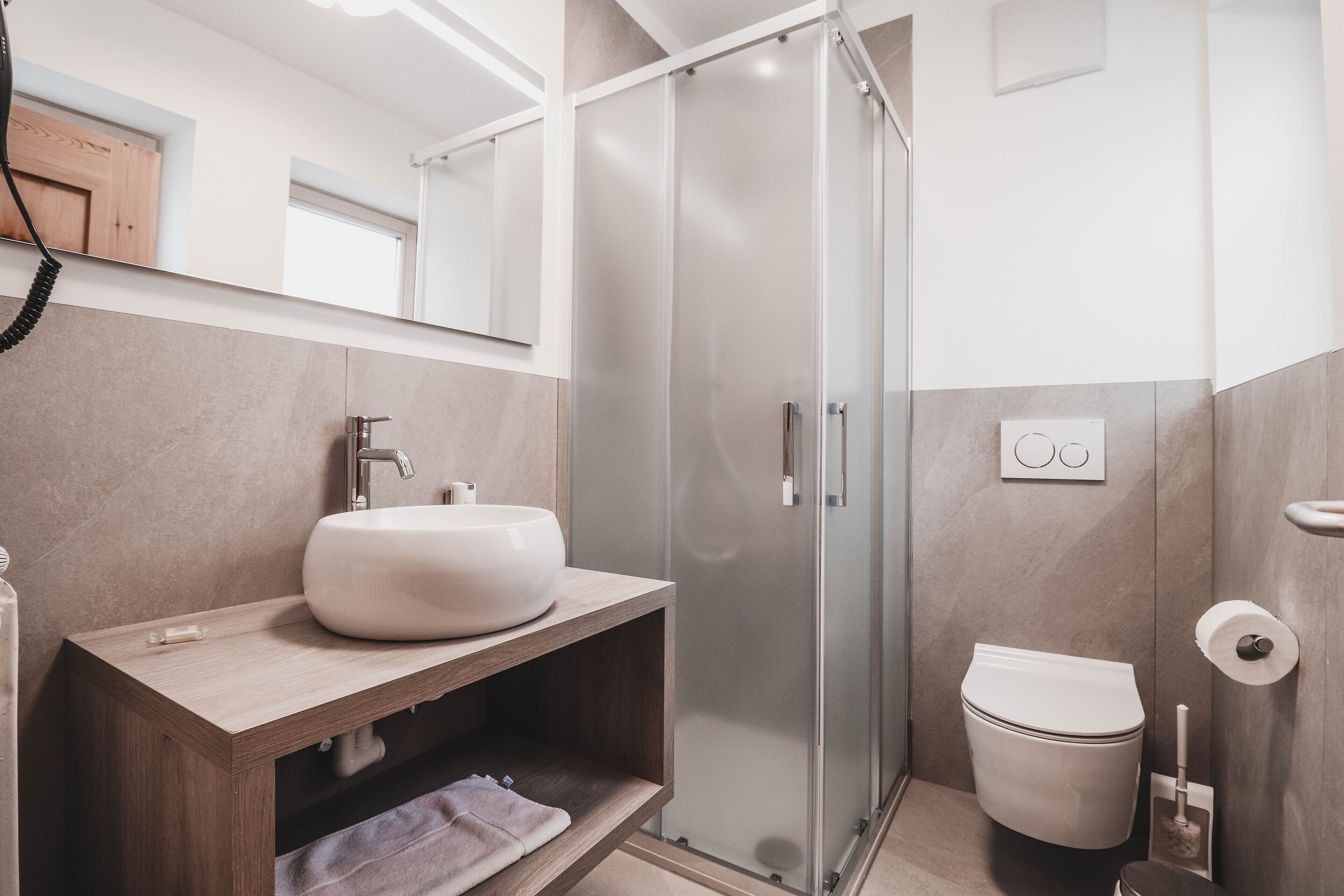 A modern bathroom with a wooden vanity, a glass shower enclosure, and a toilet.