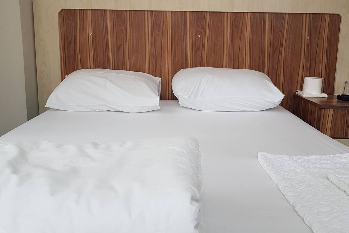 A double bed with white linens, a wooden headboard, and a nightstand with a lamp and a tissue box.