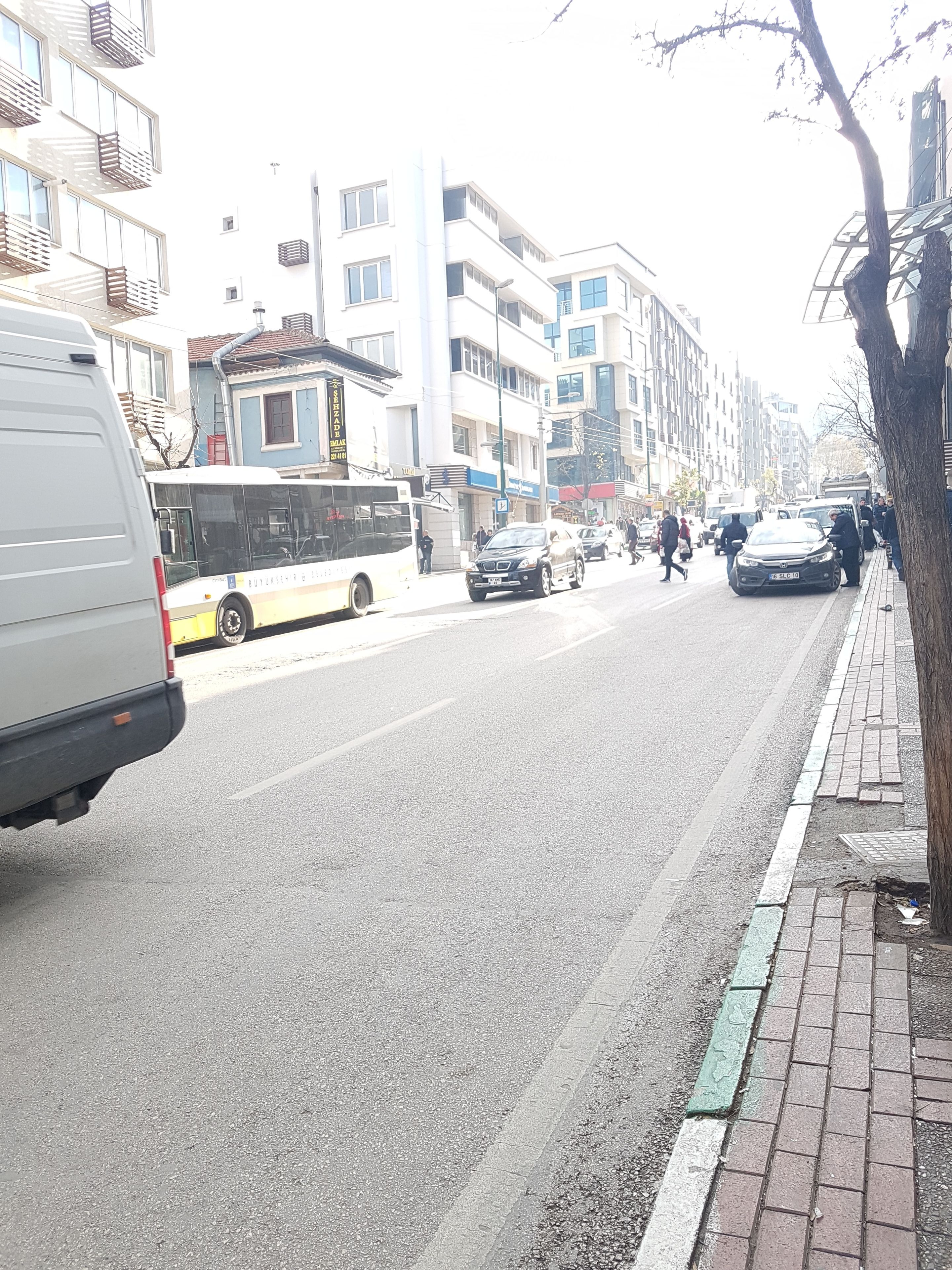 Une rue bordée d’immeubles, avec un autobus et des voitures.