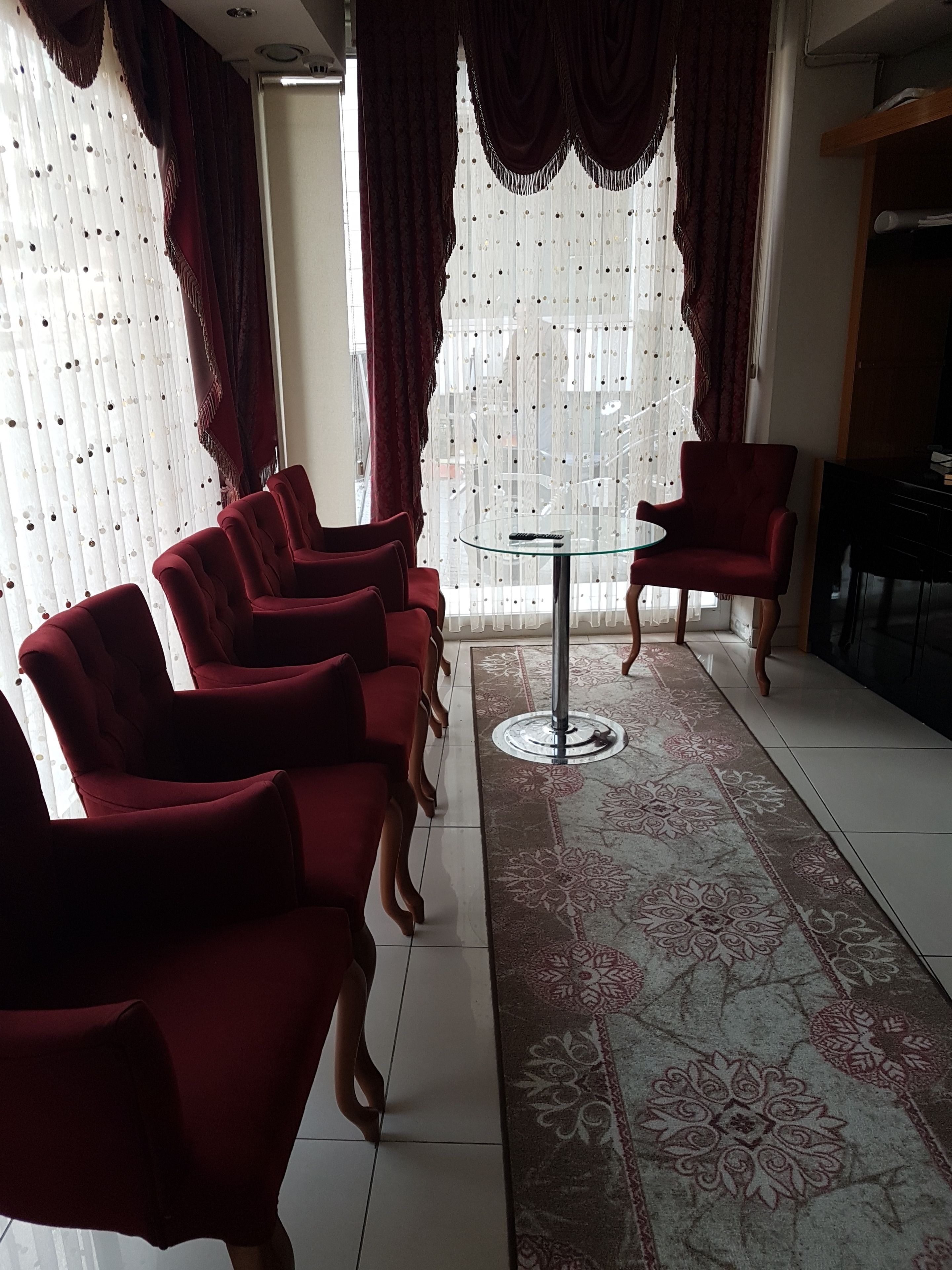 A room with a row of red chairs, a glass table, and a patterned rug.