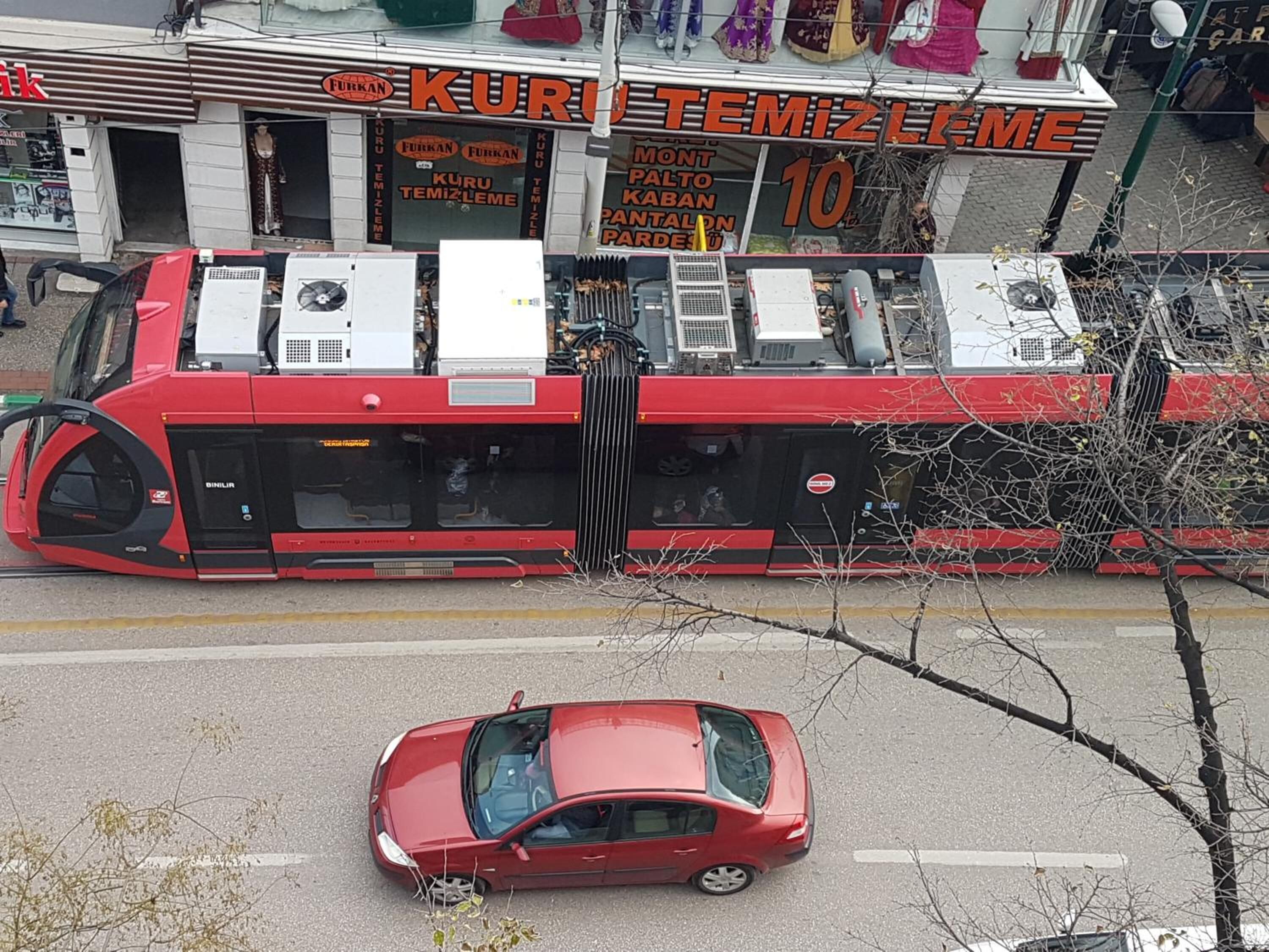 A red car driving past a building with a sign that reads "KURU TEMIZLIME" and "MONT PALTO KABAN PANTALON PARDESU".