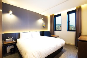 Enjoy a restful night's sleep in this cozy room with a large bed, nightstand, and table, offering a view of the city.