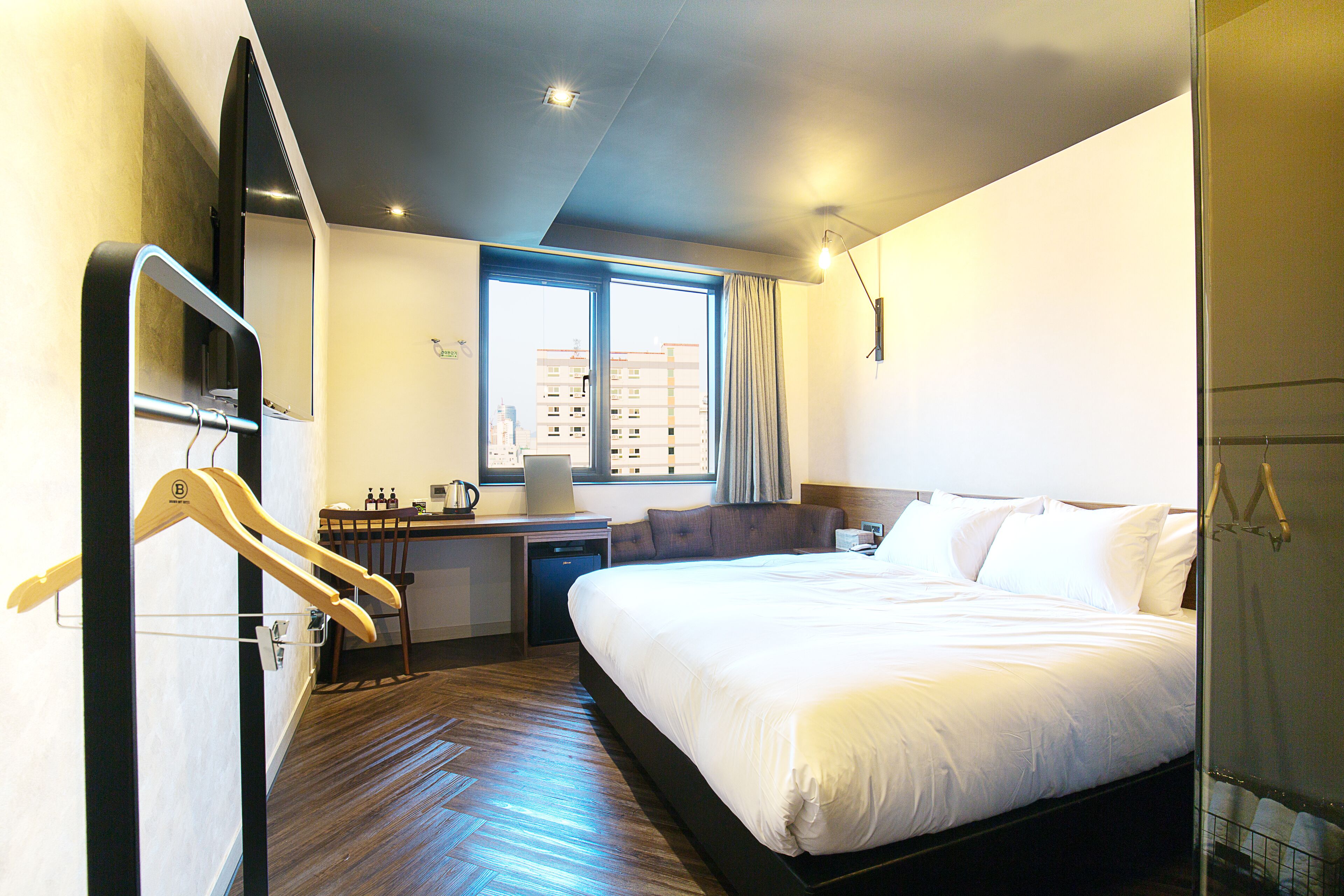 Habitación de hotel con una cama grande, un escritorio con silla, un armario y una ventana con cortinas.