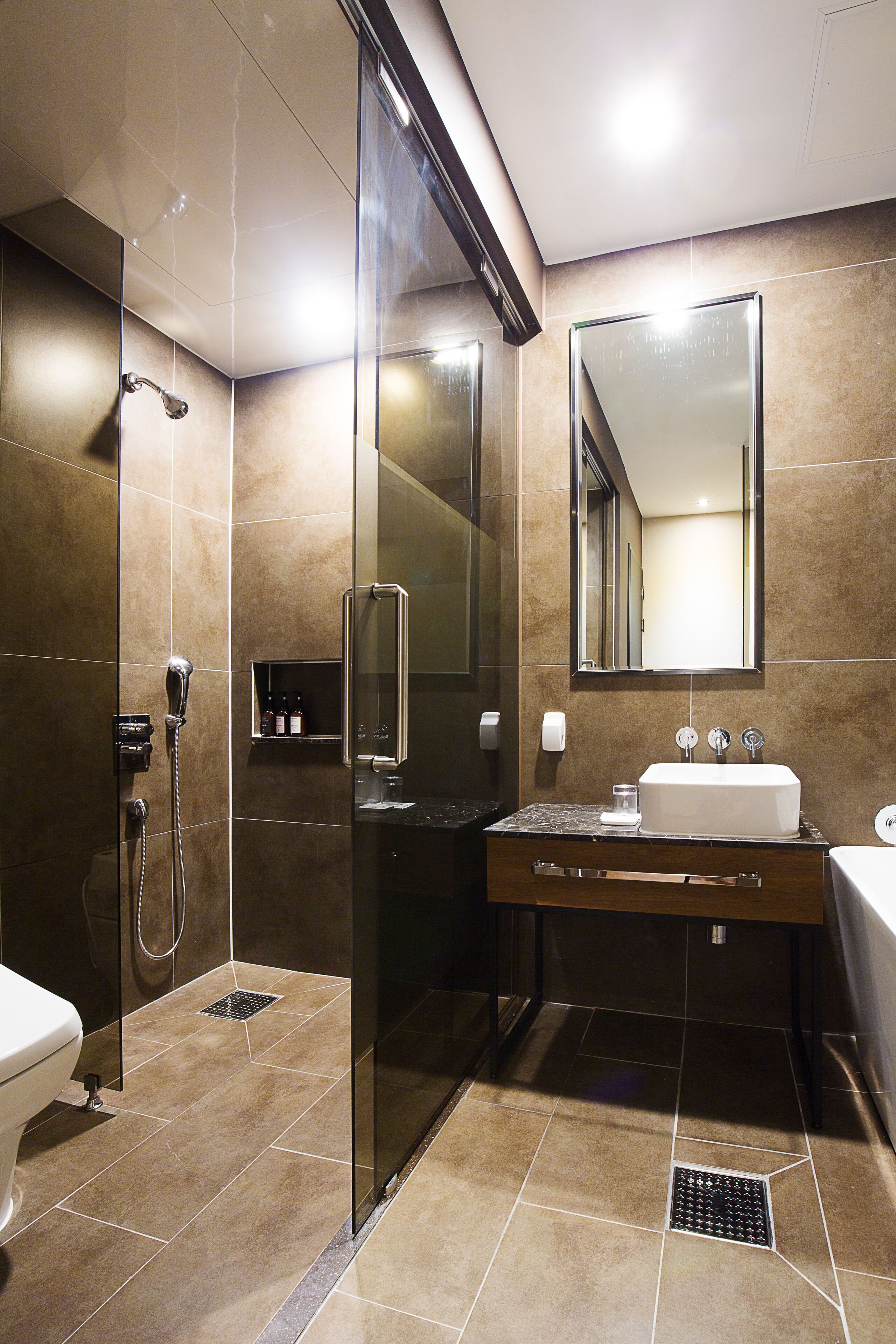 Un baño moderno con ducha de vidrio, tocador con lavamanos y un espejo grande.