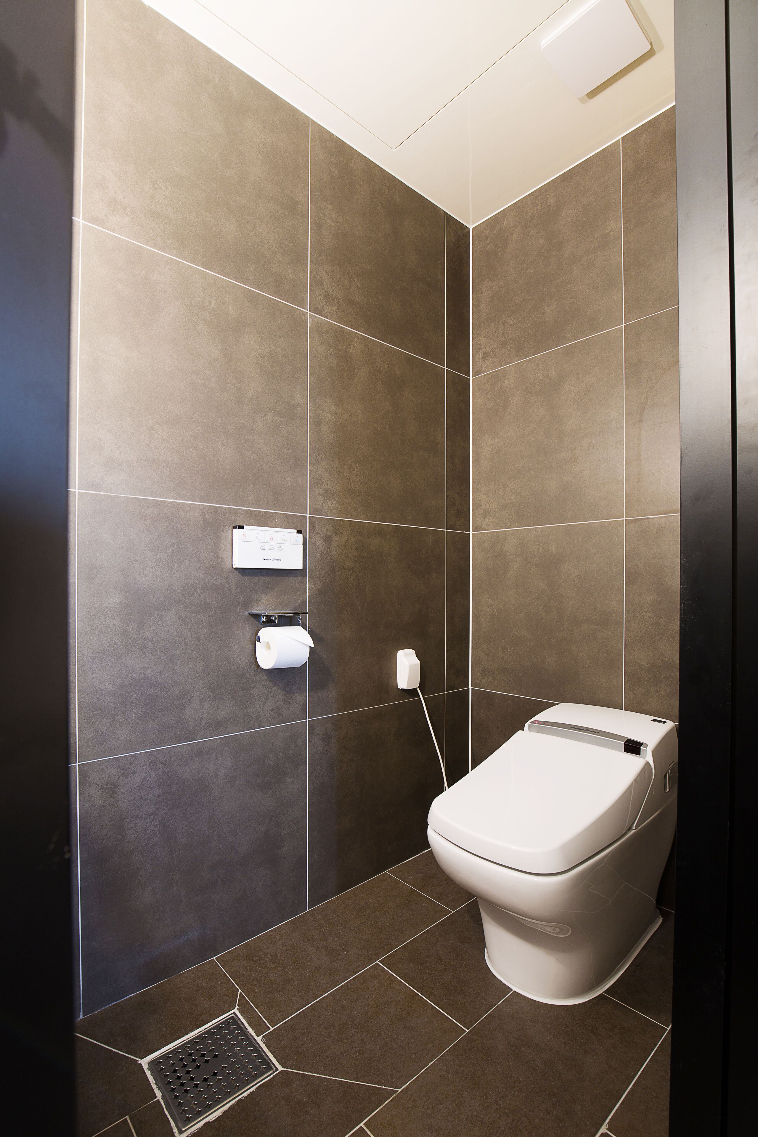 A modern bathroom with a toilet, a paper towel dispenser, and a soap dispenser mounted on the wall.