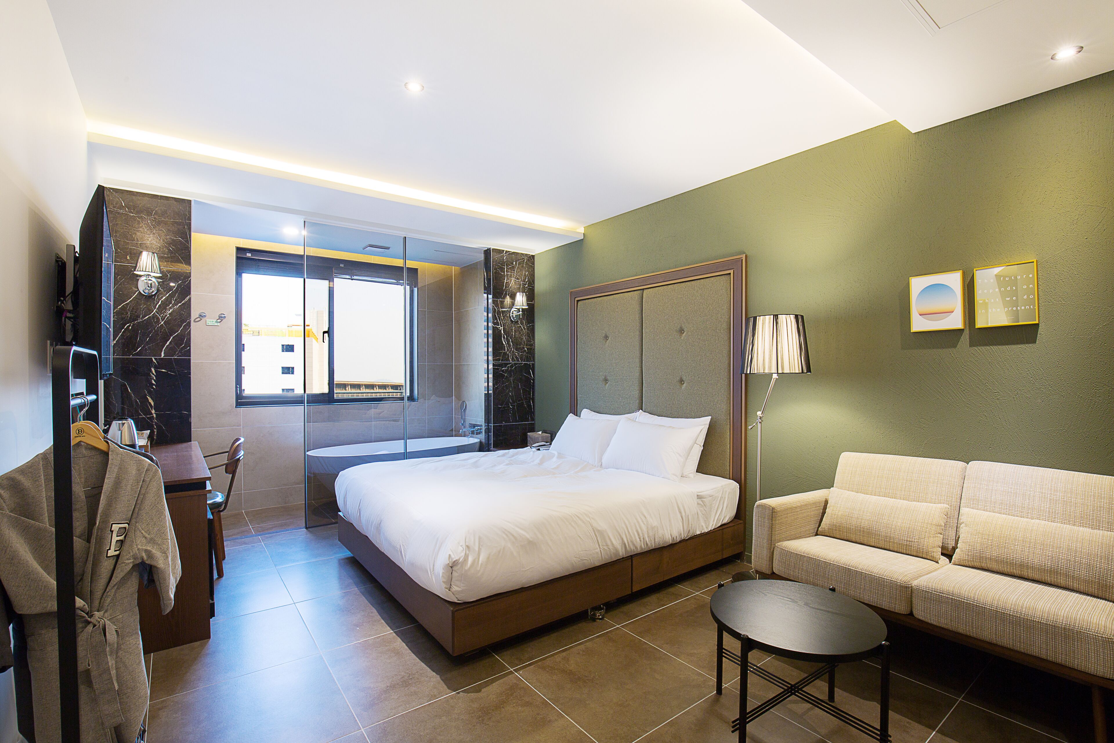 Una habitación de hotel moderna con una cama grande, un sofá, una mesita y una bata colgada en un perchero.