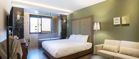 A modern hotel room with a large bed, a sofa, a small table, and a robe hanging on a rack.