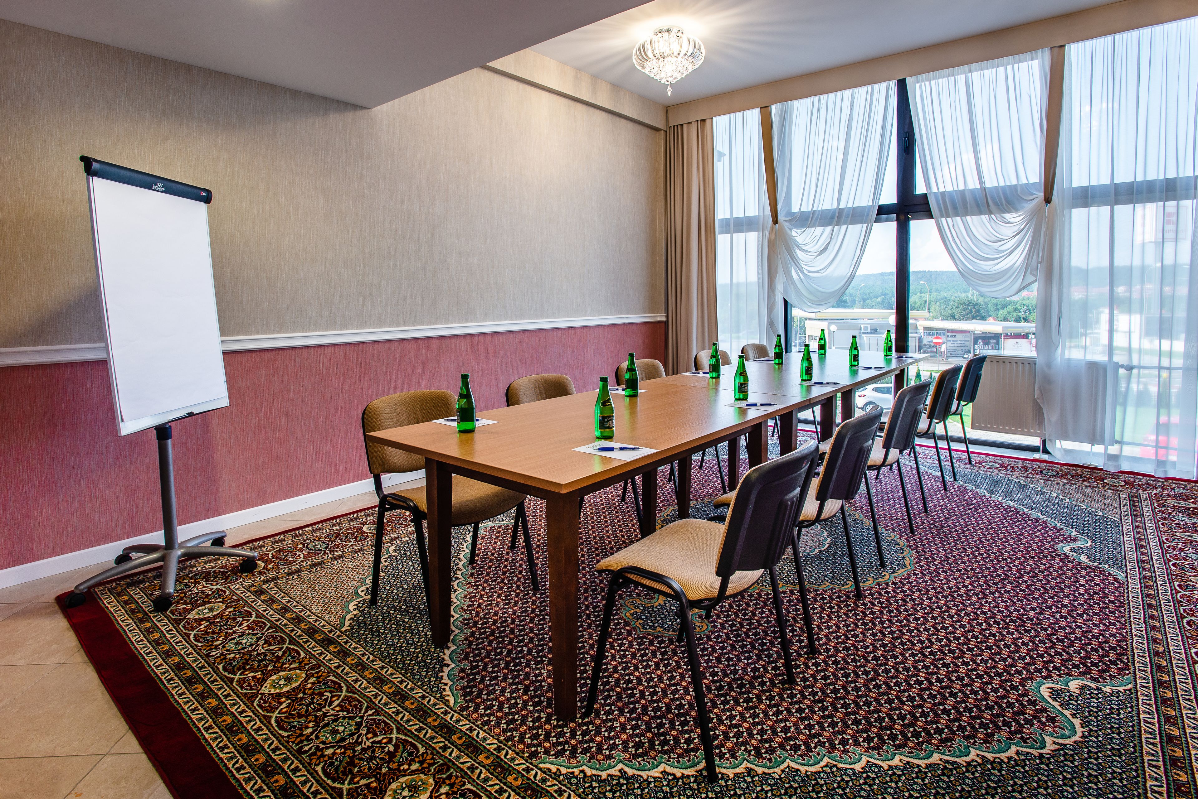 Une salle de conférence équipée d’une grande table, de chaises, d’un tableau blanc et offrant une vue sur l’extérieur grâce à de grandes fenêtres.