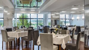 A restaurant with multiple tables set for dining, large windows offering a view of the outdoors, and a modern interior design. - Hotel La Mar (Kielce)