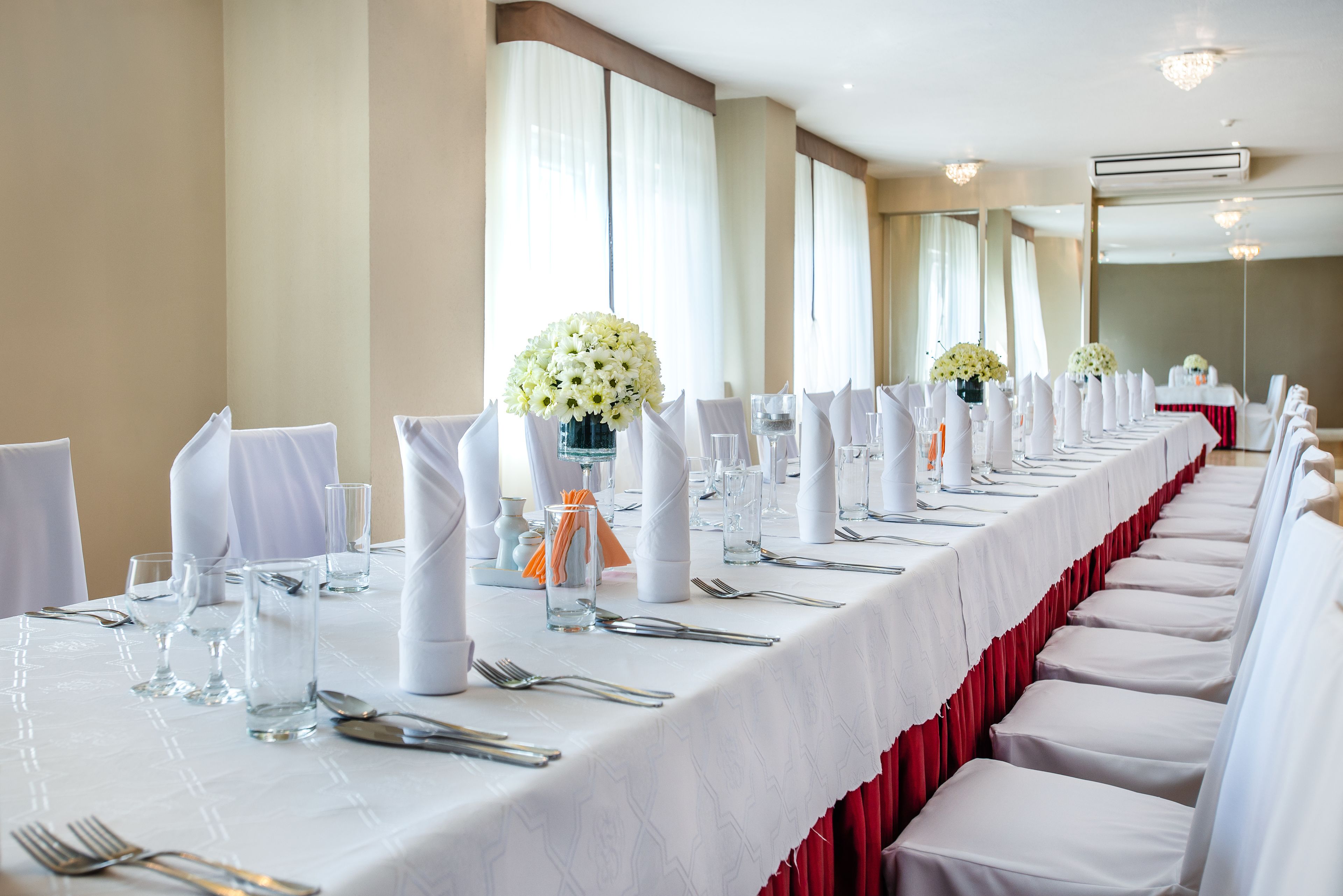 A long banquet table set with white tablecloths, red chair covers, and floral centerpieces.