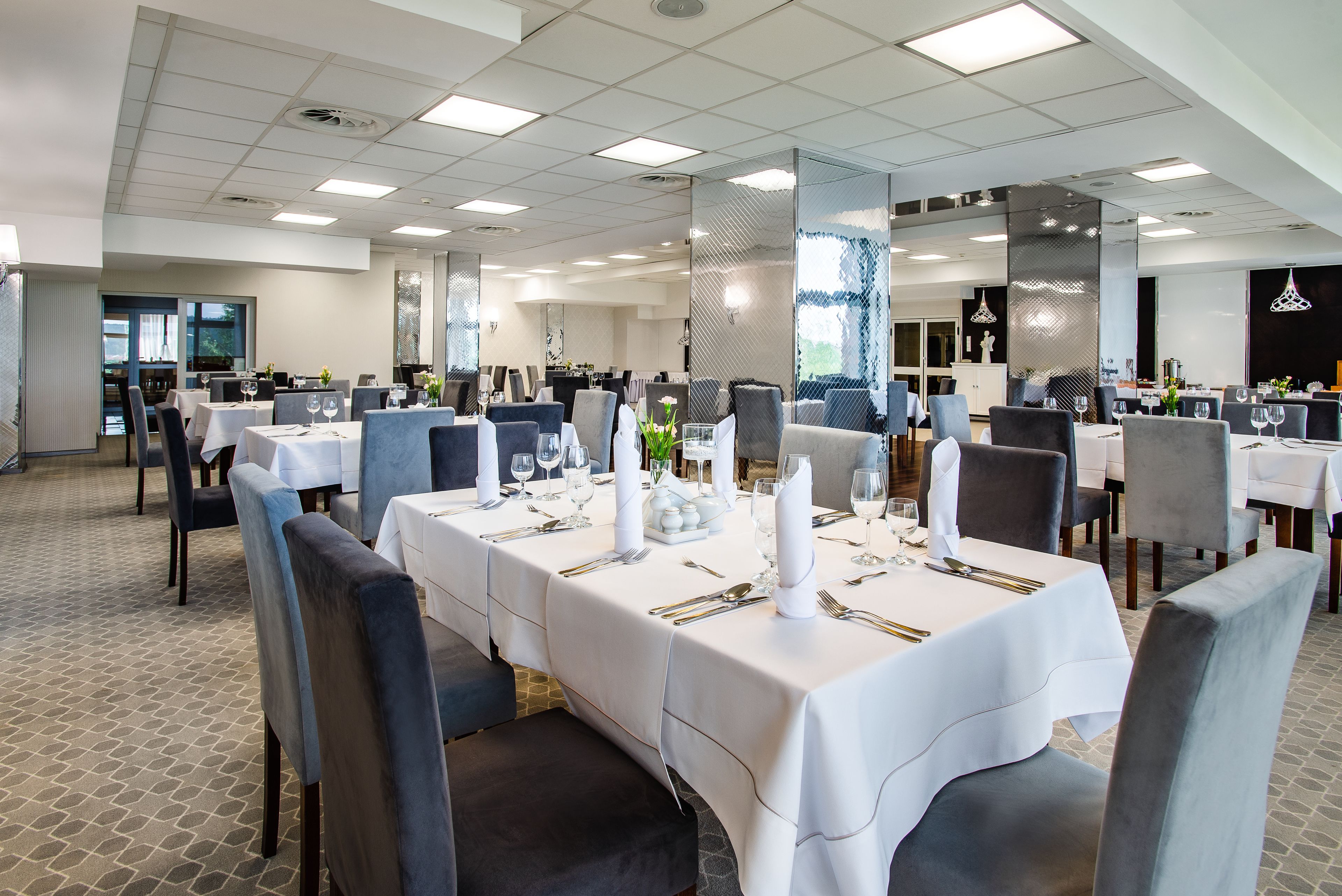 Un vaste espace dédié à la salle à manger, avec de nombreuses tables dressées pour le service, et un intérieur au design épuré et moderne.