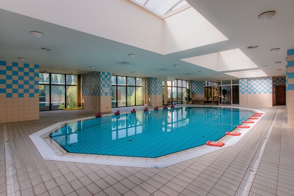 Una piscina interior con paredes a cuadros, ventanas amplias y suelo de baldosas.