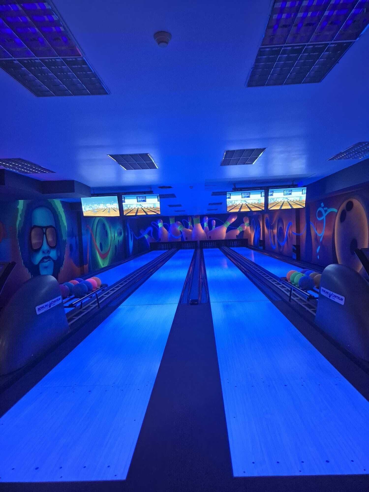 Una bolera con varias pistas, bolos y luces colgantes.